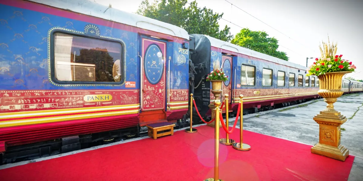 A folk dancer welcoming guests beside the blue, Warli-painted livery of the Deccan Odyssey