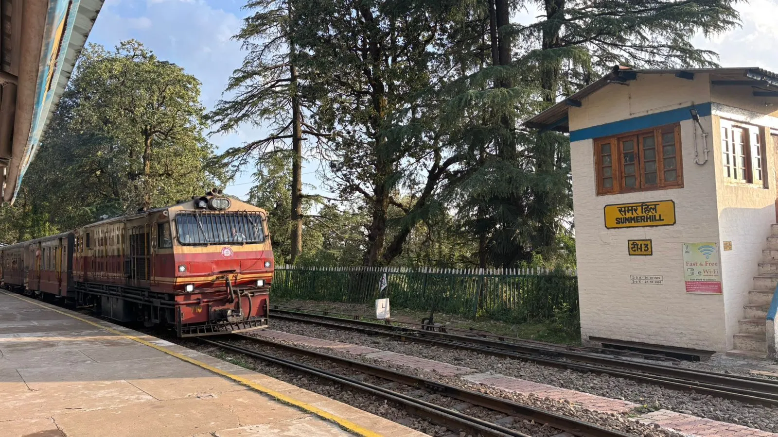A maroon train at the heritage Summer Hill station on the Kalka-Shimla Railway, among pines