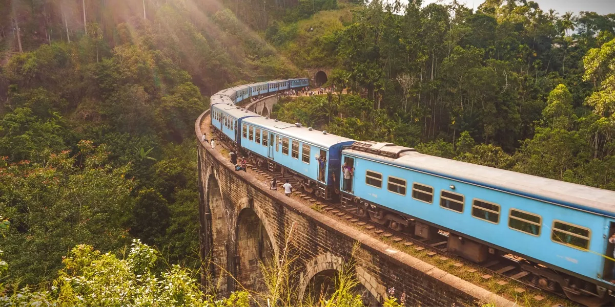 A red Sri Lankan hill-country train winding through terraced tea estates between Kandy and Ella