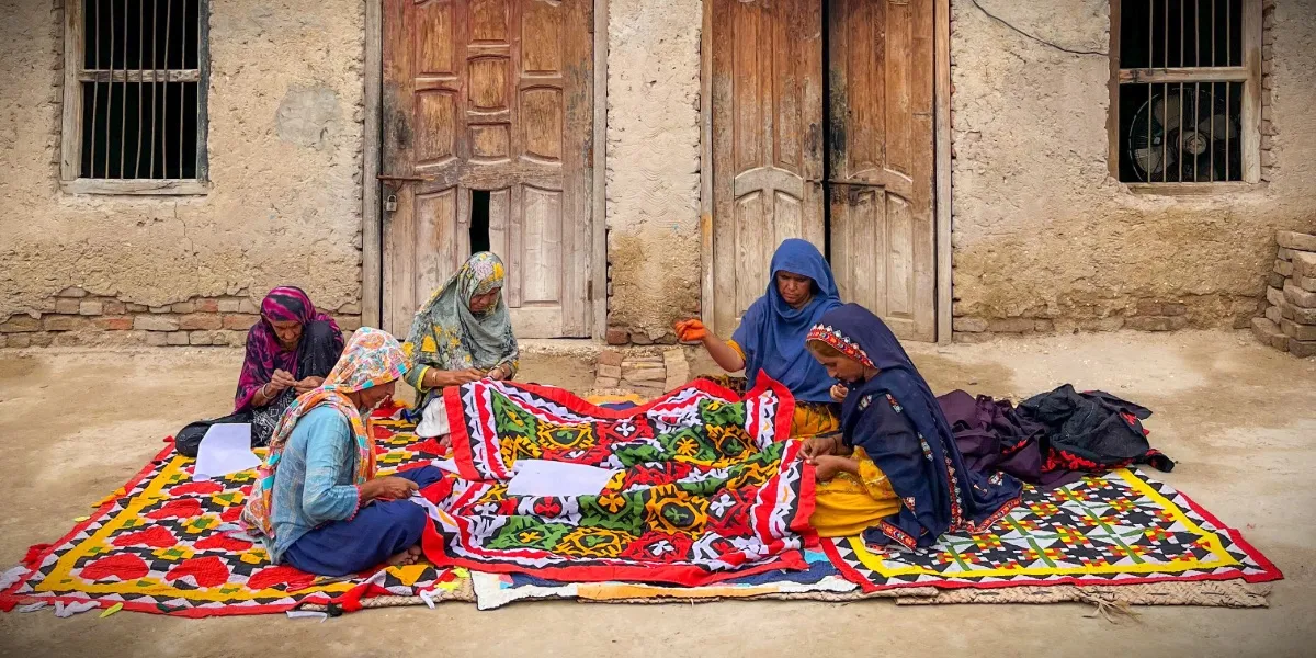 A woman seated before a display of brightly coloured embroidered fabrics