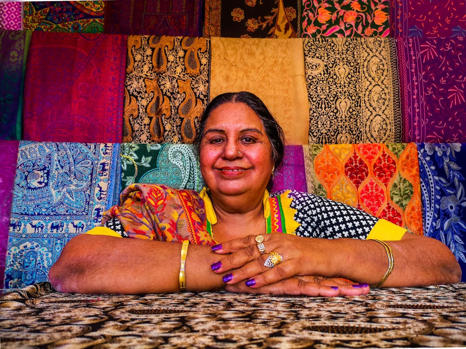 A woman seated before a display of brightly coloured embroidered fabrics