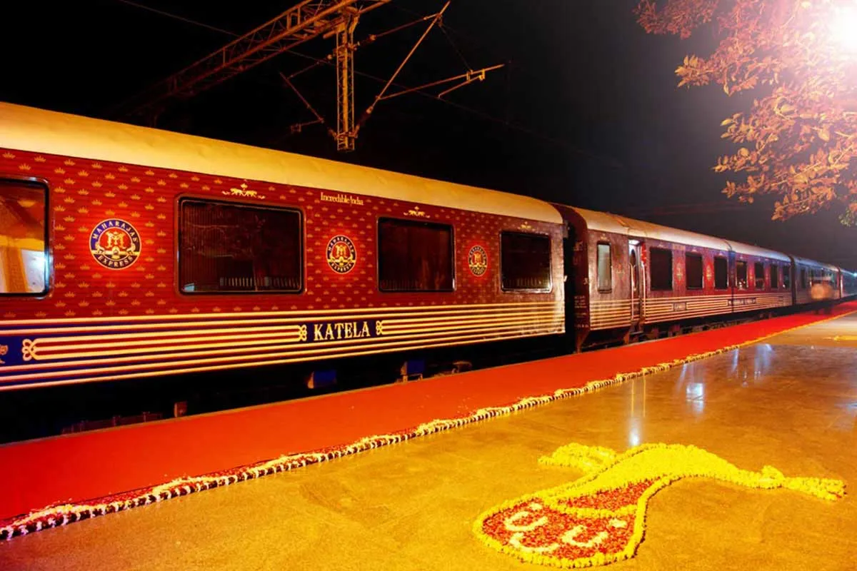 The deep-red and gold carriages of the Maharajas' Express beside a flower-decorated platform at night