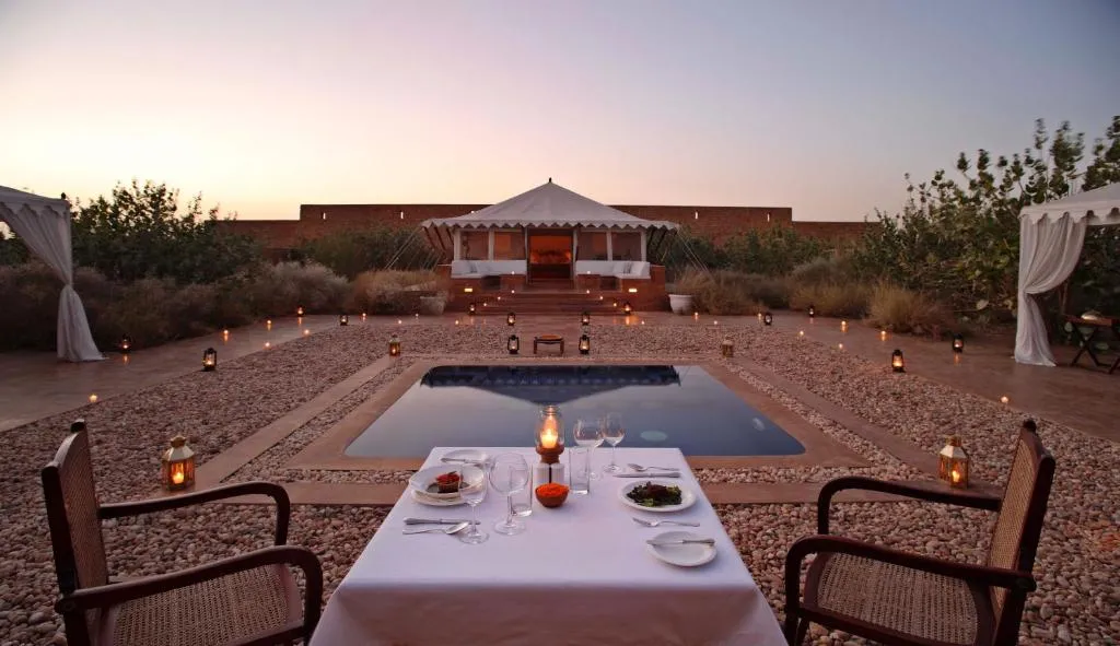A candlelit private dinner beside a pool, with a ceremonial tent pavilion beyond, at dusk in Rajasthan