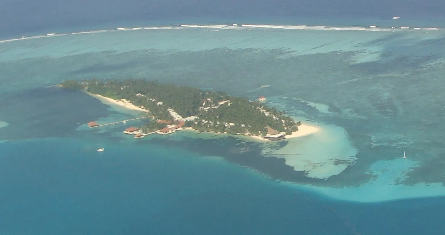 An aerial view of a Maldivian island ringed by a turquoise lagoon and reef